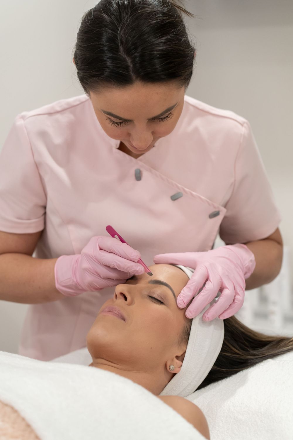 Aesthetician in pink uniform performing facial treatment on relaxed client.