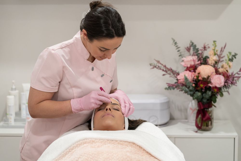 Spa professional performing facial procedure with floral arrangement in background.