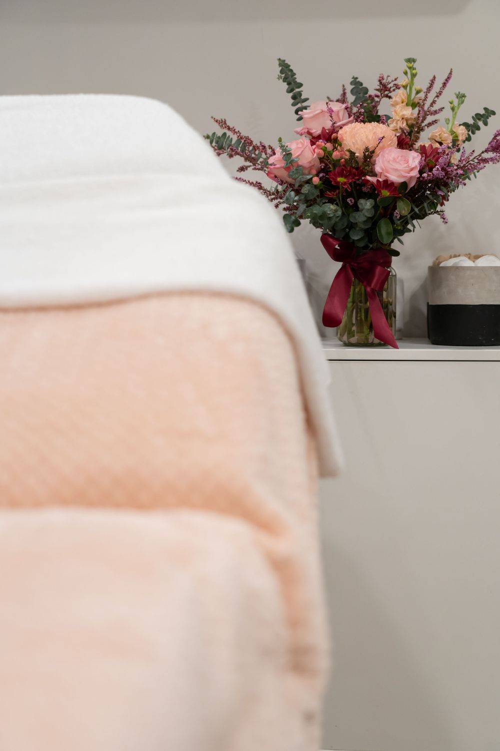 Peaceful spa setting with pink floral arrangement next to treatment bed.