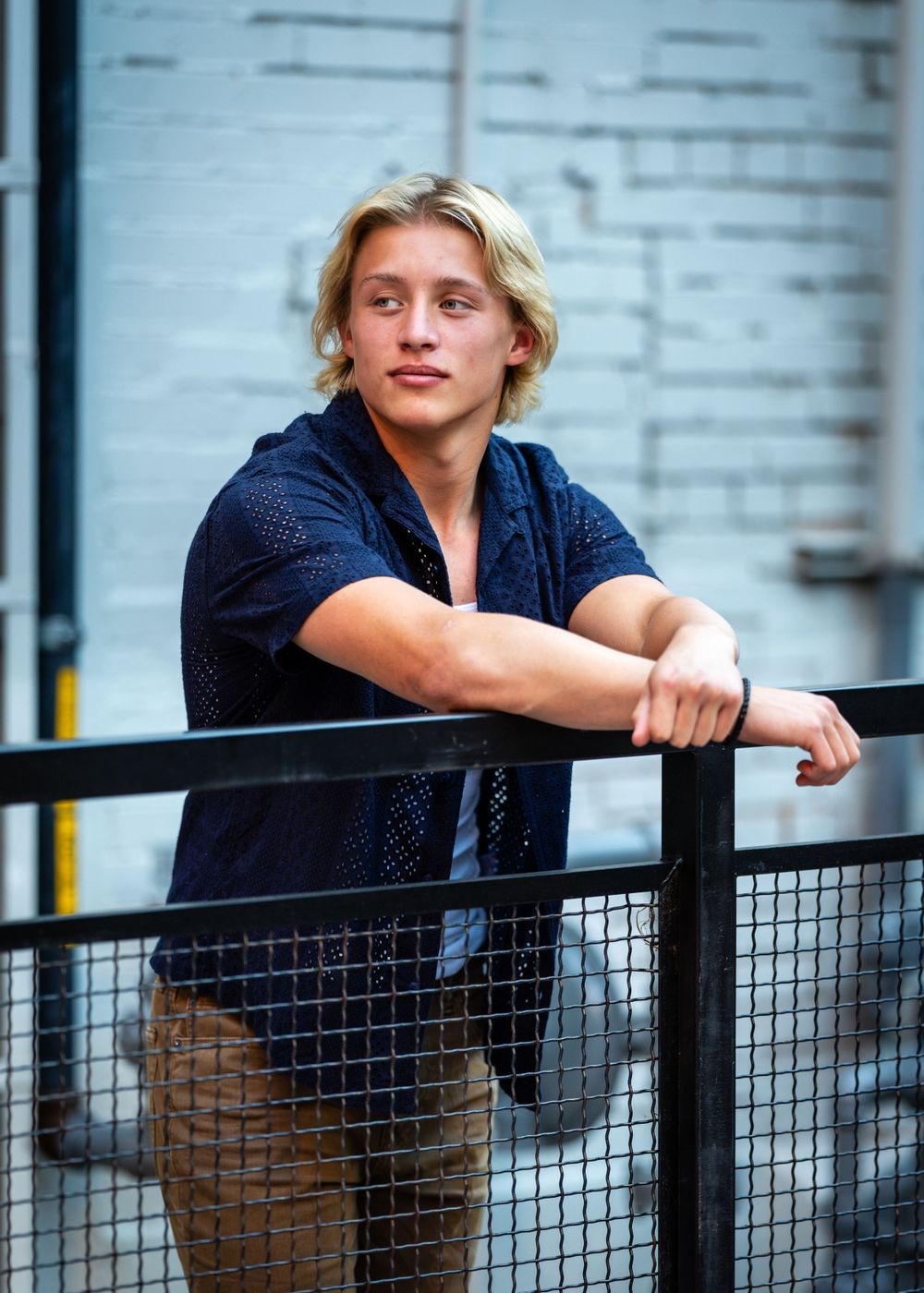 Young person in navy shirt leans on metal railing in casual pose.