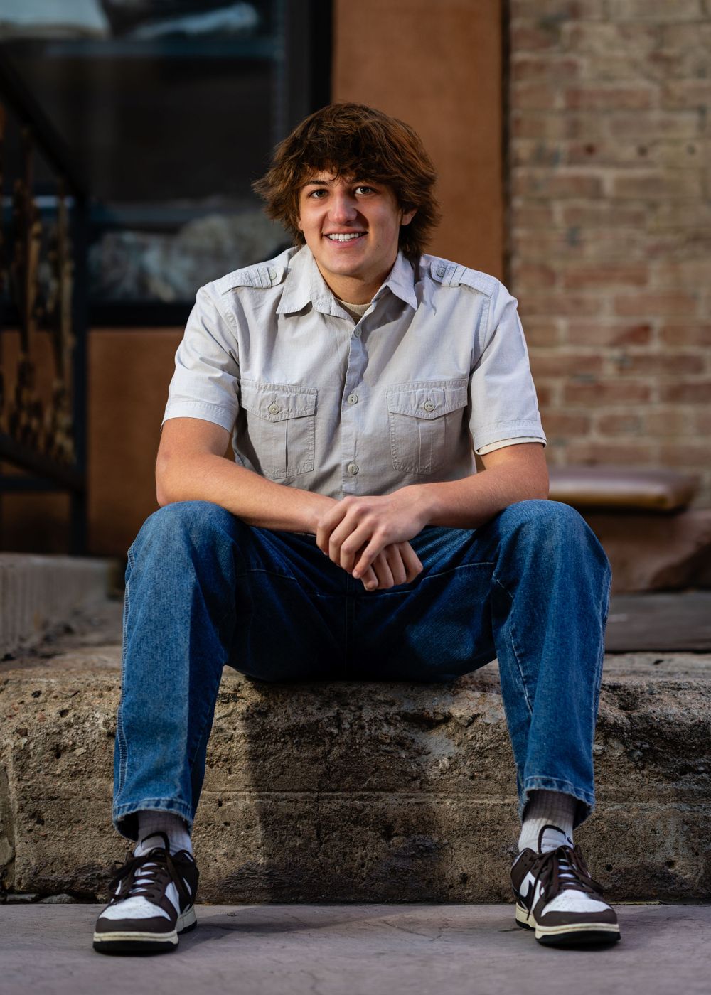 Portrait of casually dressed student sitting on concrete steps near brick wall.