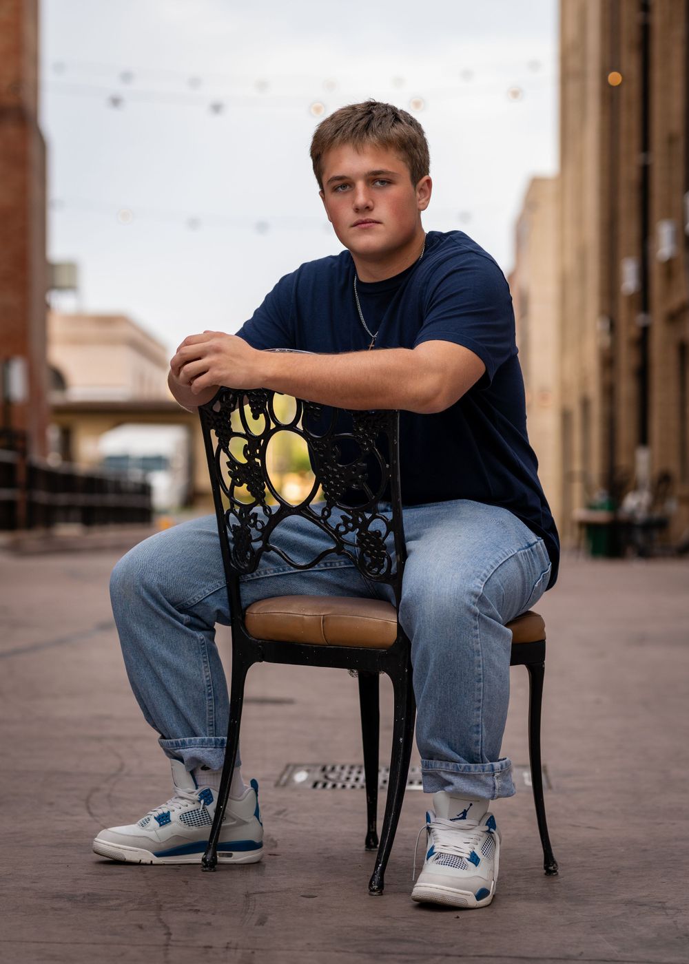 Portrait of a student seated on a metal chair outdoors in a blue shirt and jeans.