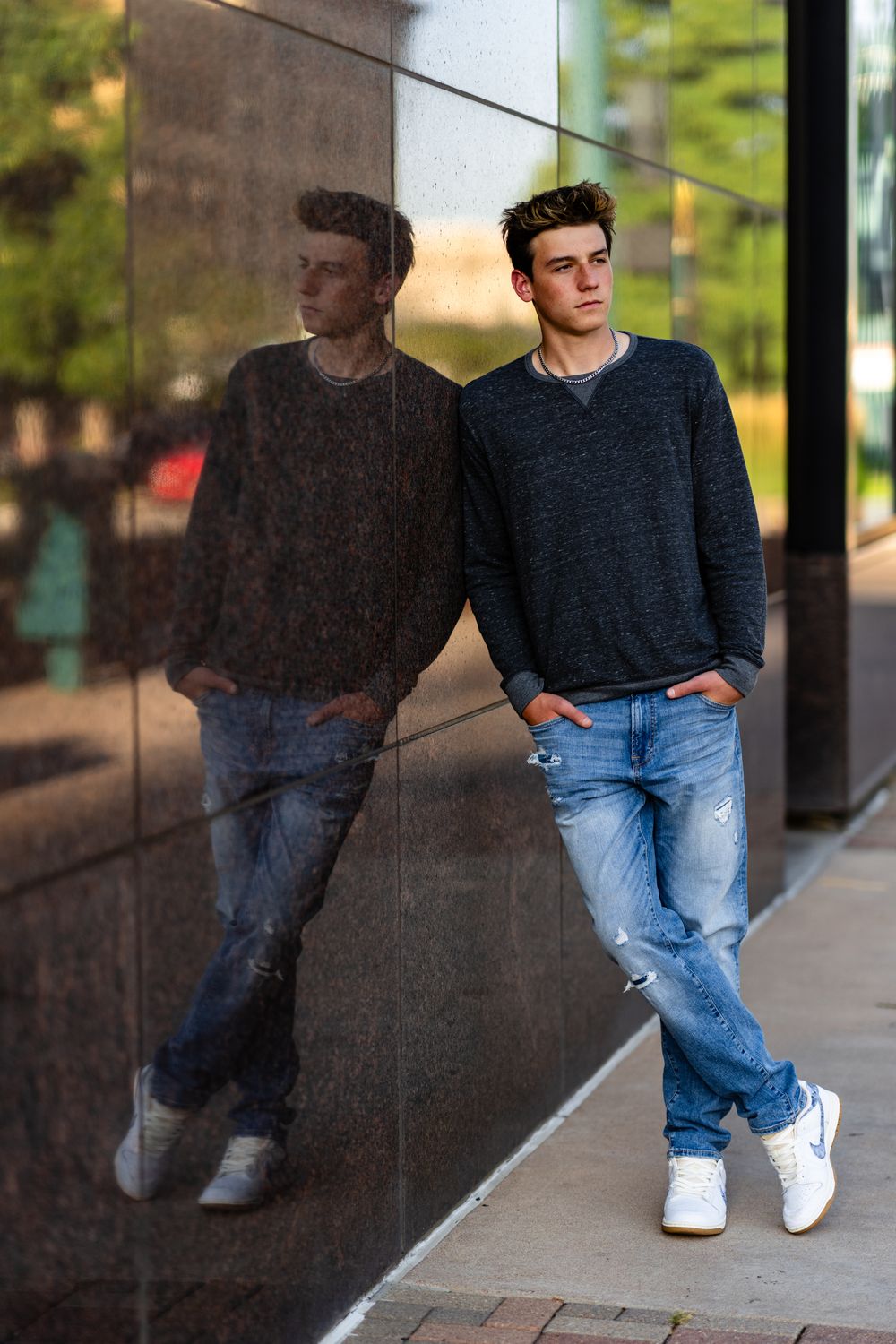 Person in navy sweater leans against reflective wall creating mirror effect.