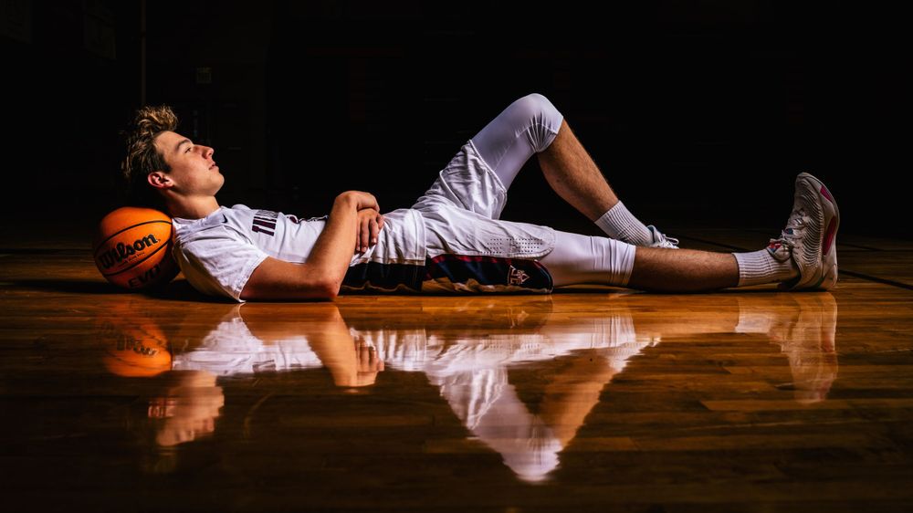 Basketball player lying on reflective court surface with dramatic lighting.