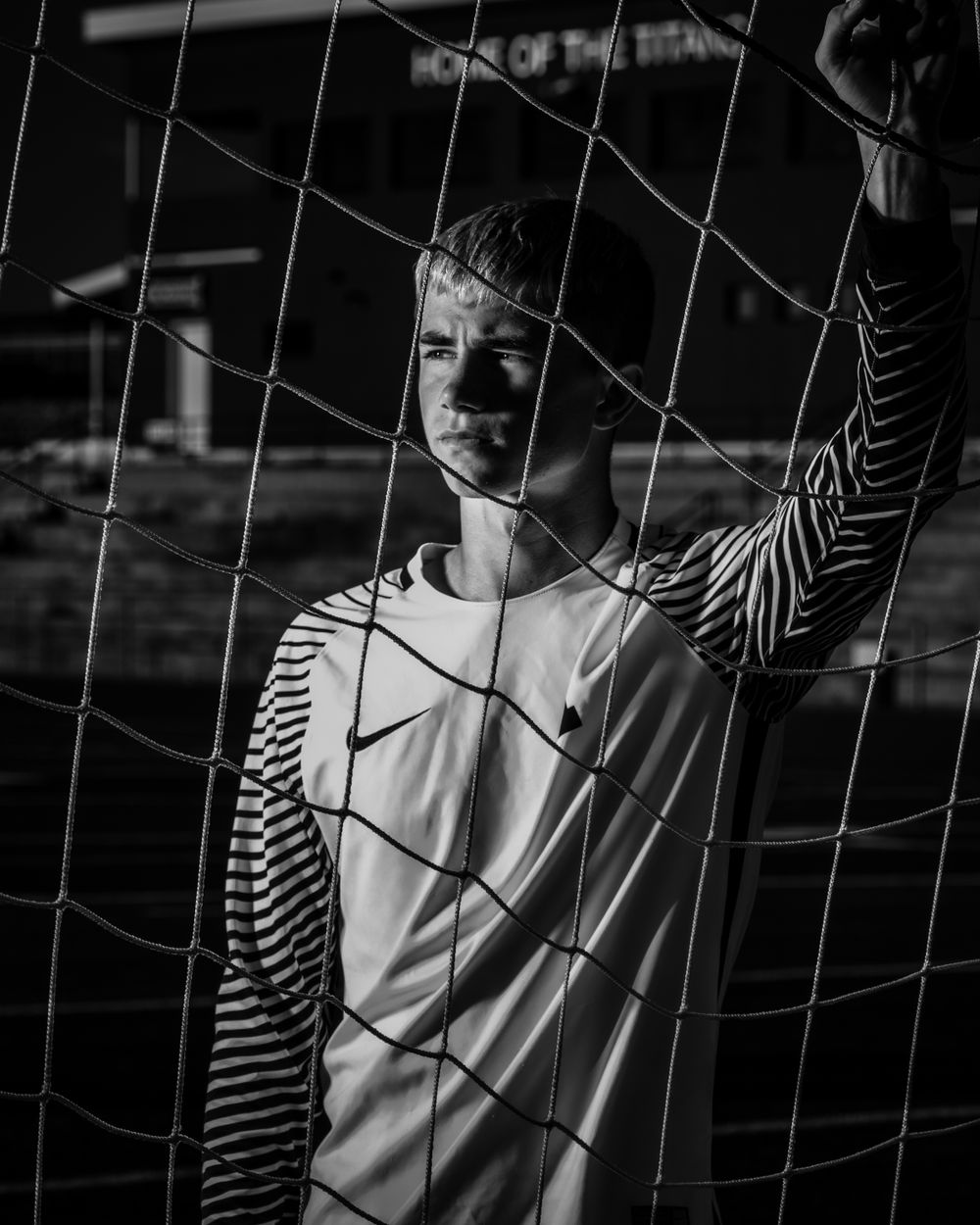 Artistic black and white portrait of goalkeeper behind soccer net.