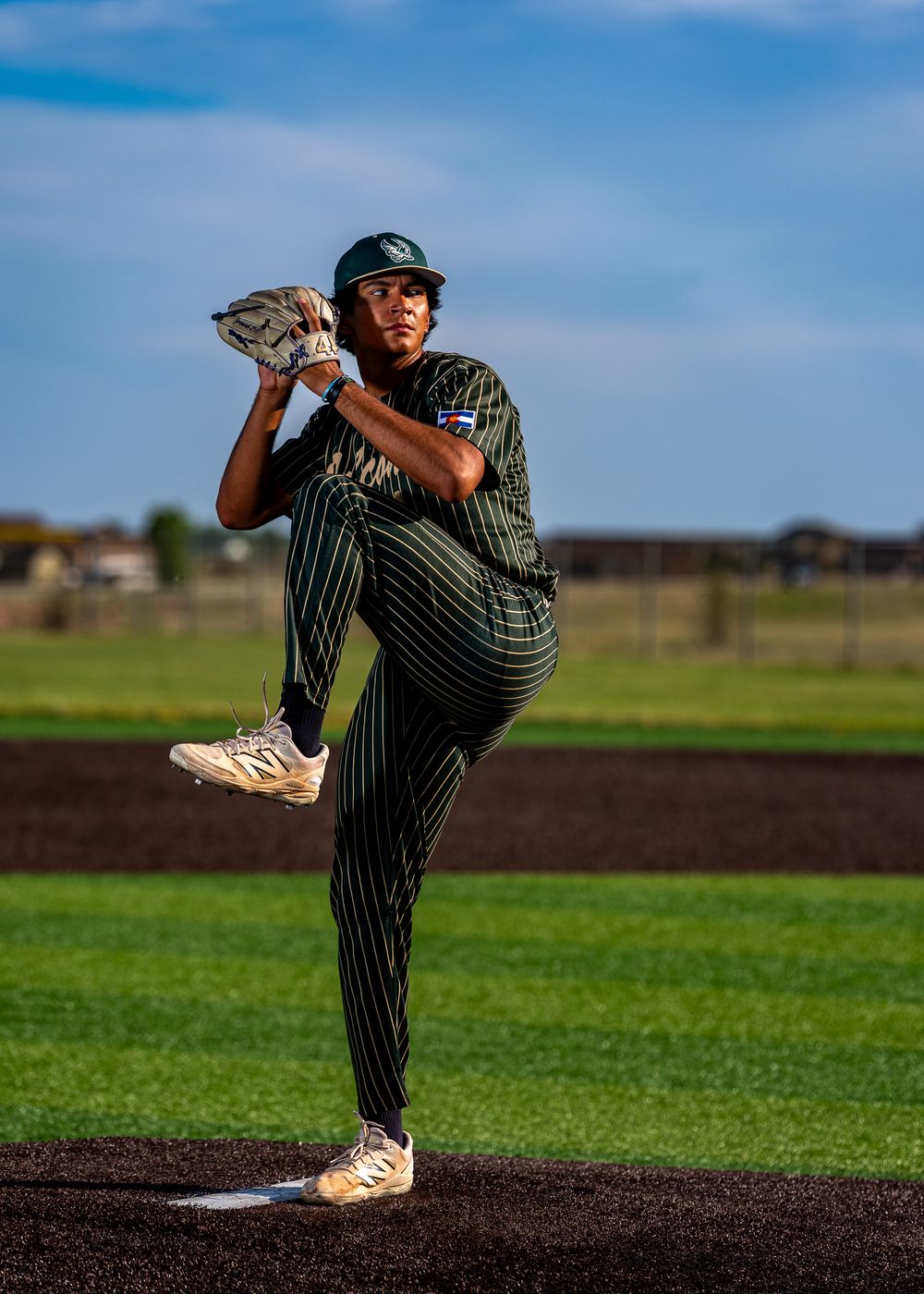 Baseball pitcher in green pinstripe uniform mid-windup on mound under blue sky on a sunny day.