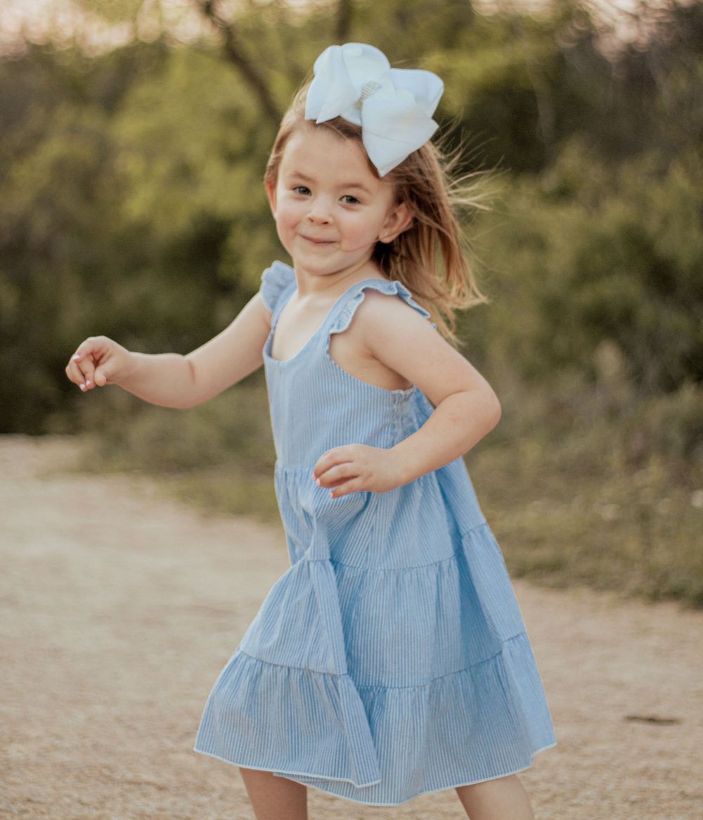 A little one dances and twirls in a blue and white striped ruffle dress with matching bow outdoors.