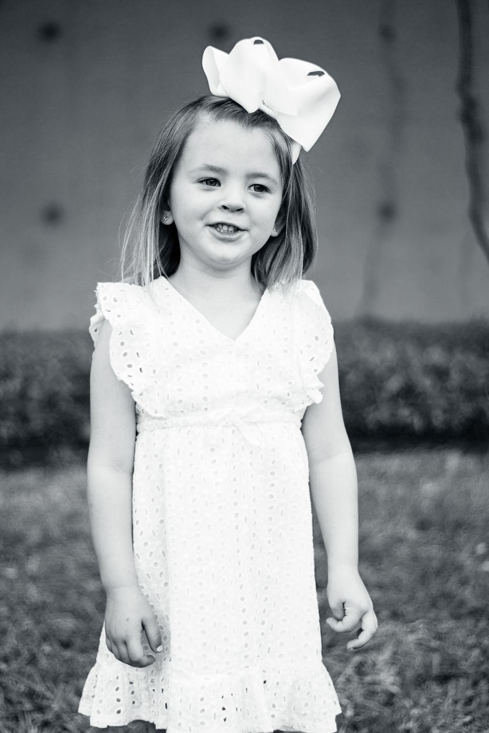 Black and white portrait of a young child in a white eyelet dress and large bow hair accessory.