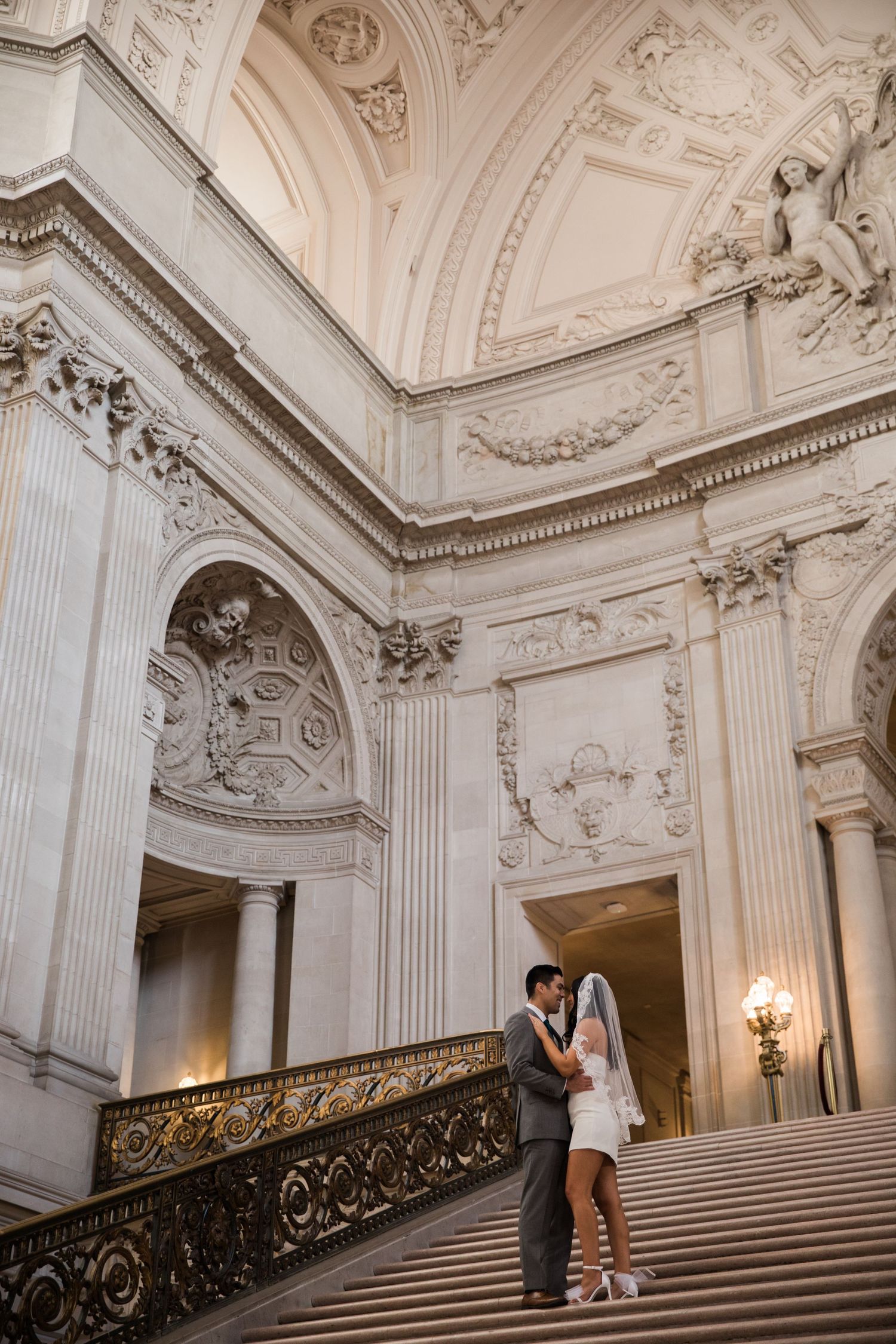 Married Bride and Groom after a San Francisco City Hall civil ceremony, standing on the grand stair case kissing.