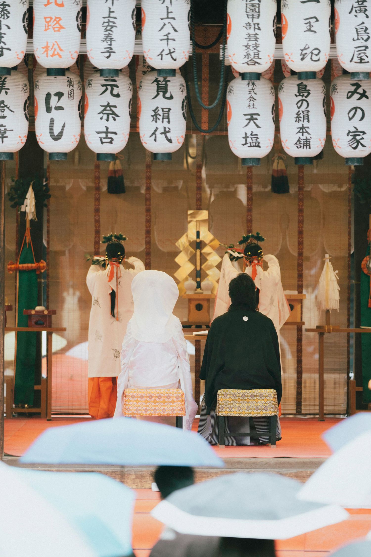 Traditional Japanese Shinto wedding ceremony at a shrine with lanterns and guests holding umbrellas.