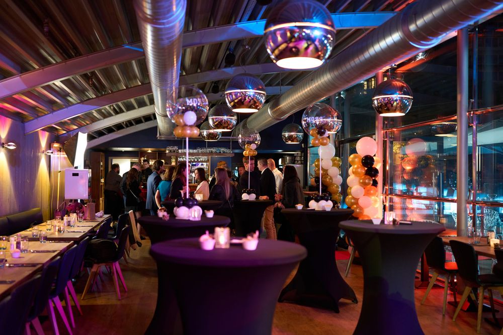 Aménagement élégant d'une salle de fête avec éclairage violet, tables à cocktail et luminaires décoratifs au plafond.