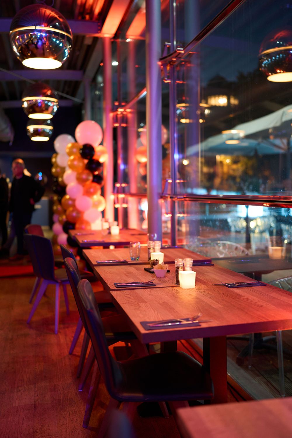 Intérieur de restaurant moderne avec tables en bois et ballons roses éclairés par des suspensions créant une atmosphère intime.