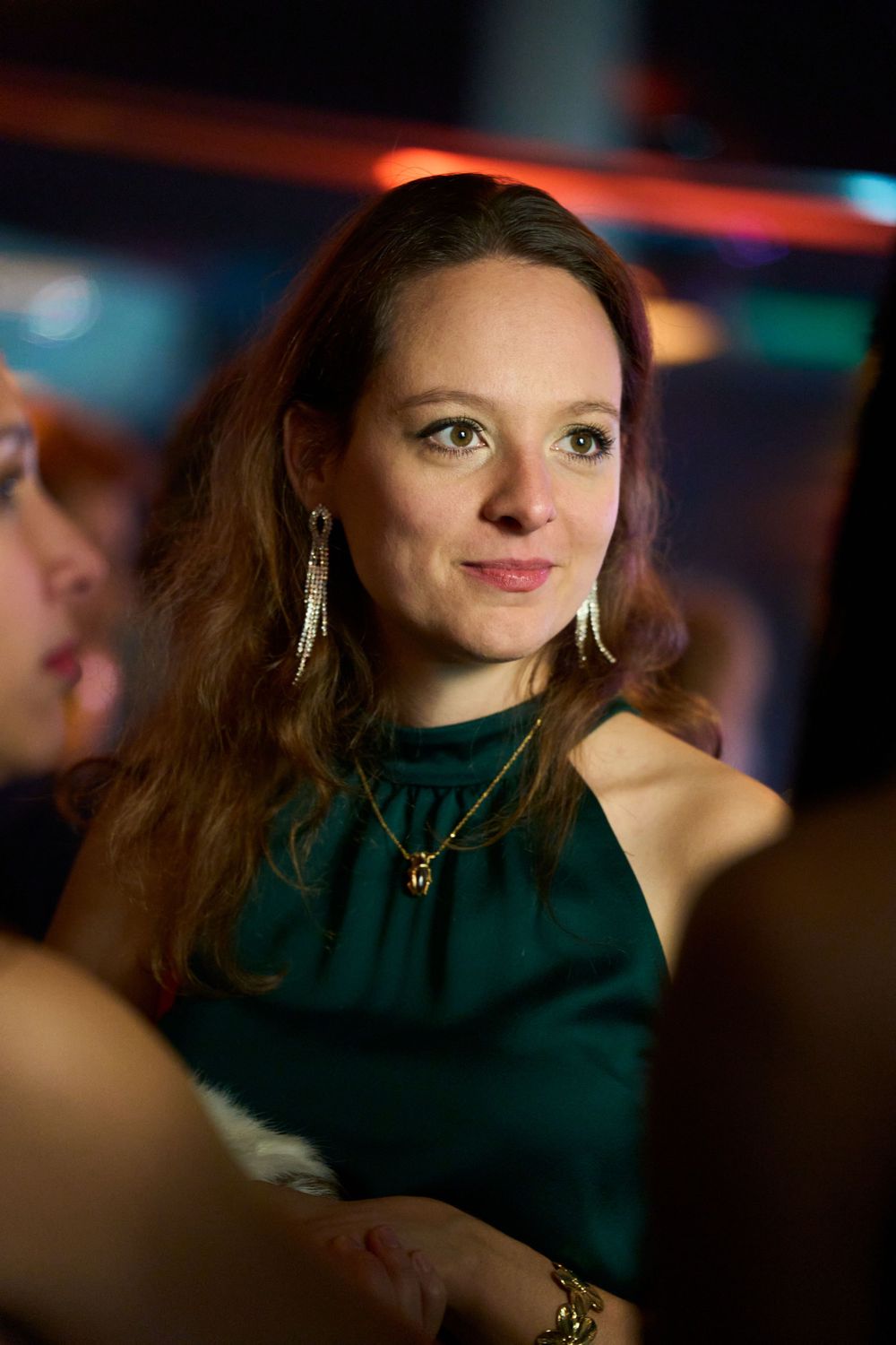 Participante élégante en robe vert émeraude avec boucles d'oreilles pendantes lors d'une soirée.