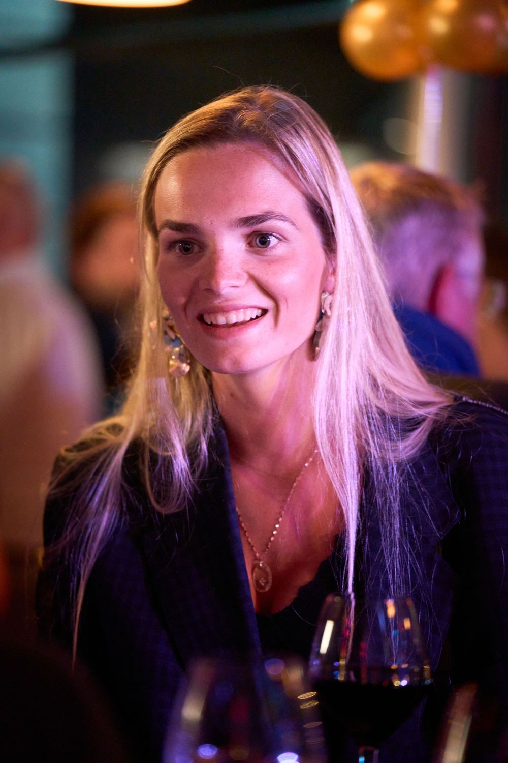 Portrait d'un invitée élégante à l'événement portant des vêtements sombres et des bijoux sous un éclairage d'ambiance.