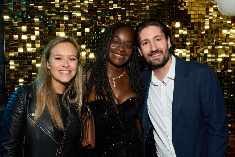 Les invités d'une fête posent devant un fond scintillant de paillettes dorées lors d'une soirée de célébration.