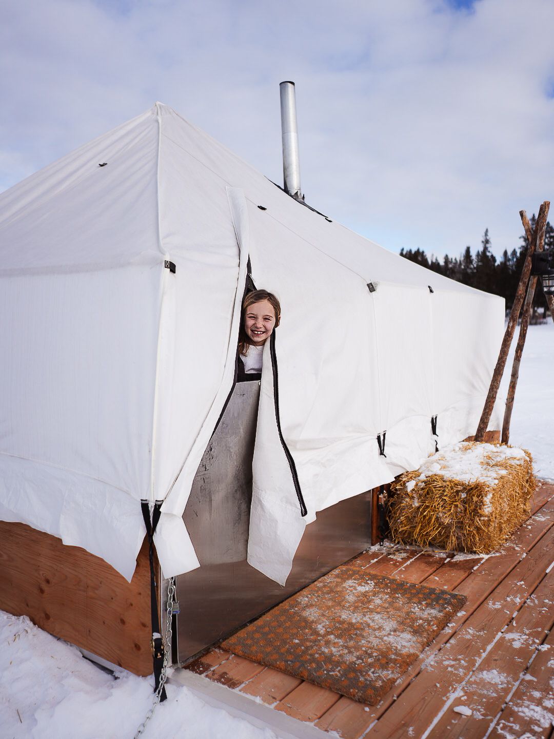 White tent exterior with hay bales and wooden posts in snowy conditions.