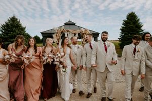 Wedding party in beige suits and rose-colored dresses pose together outdoors.