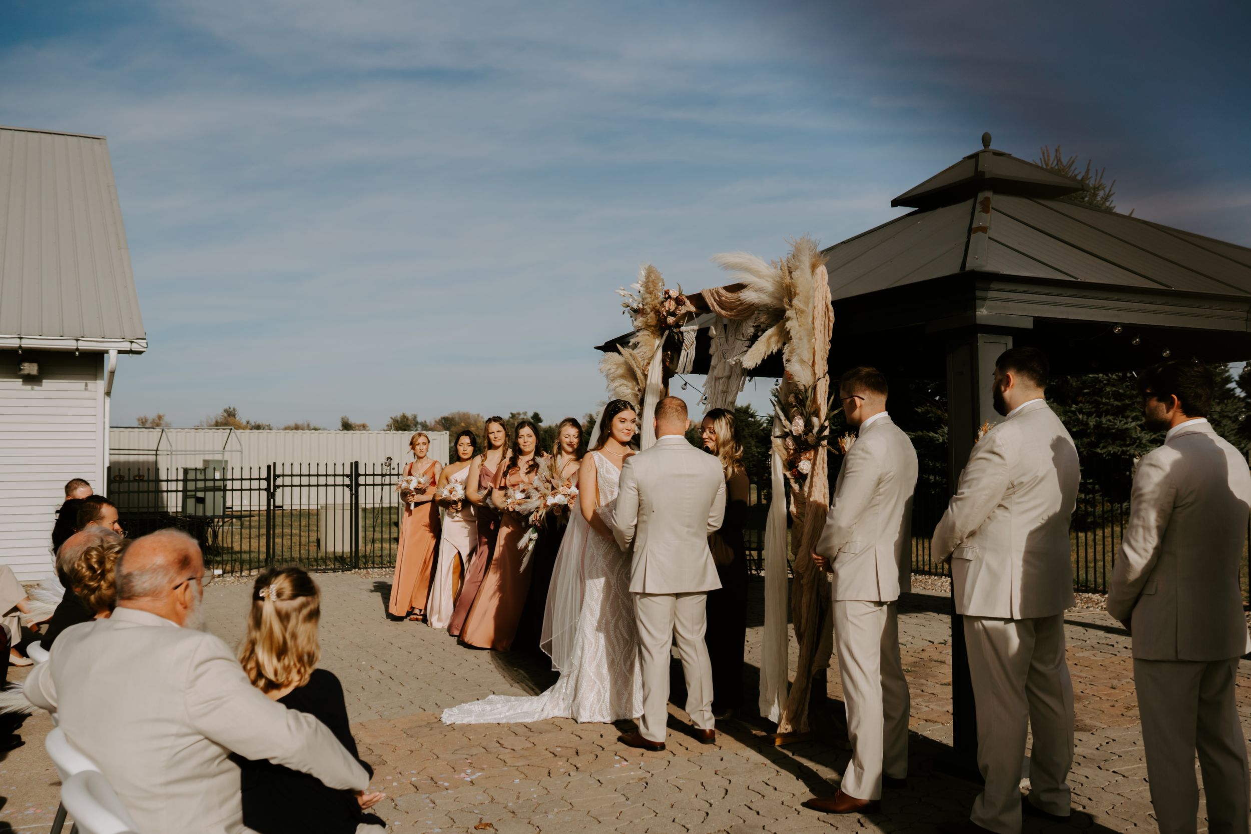 Wedding guests gather outdoors under blue skies for a celebration.