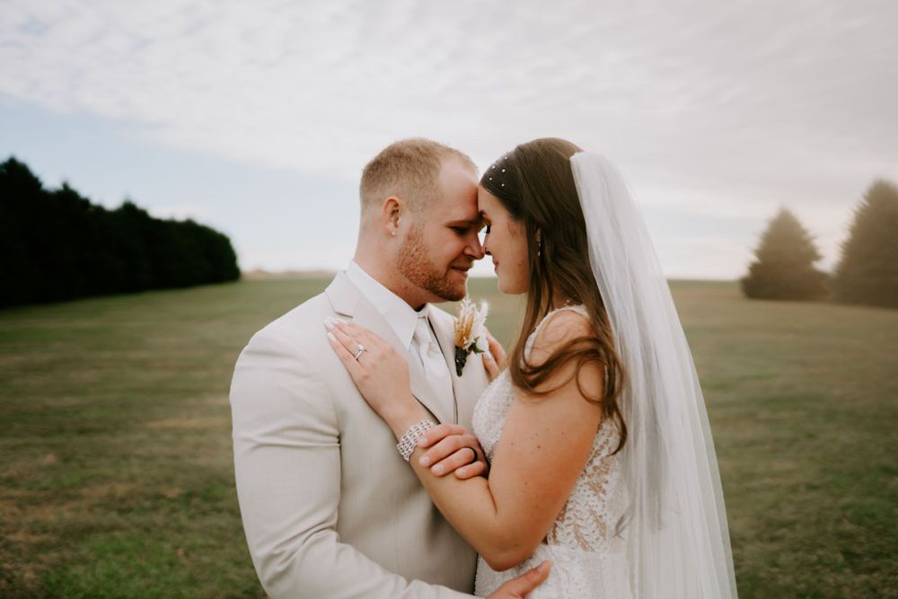 Romantic wedding couple embraces in a sunlit outdoor field during golden hour.