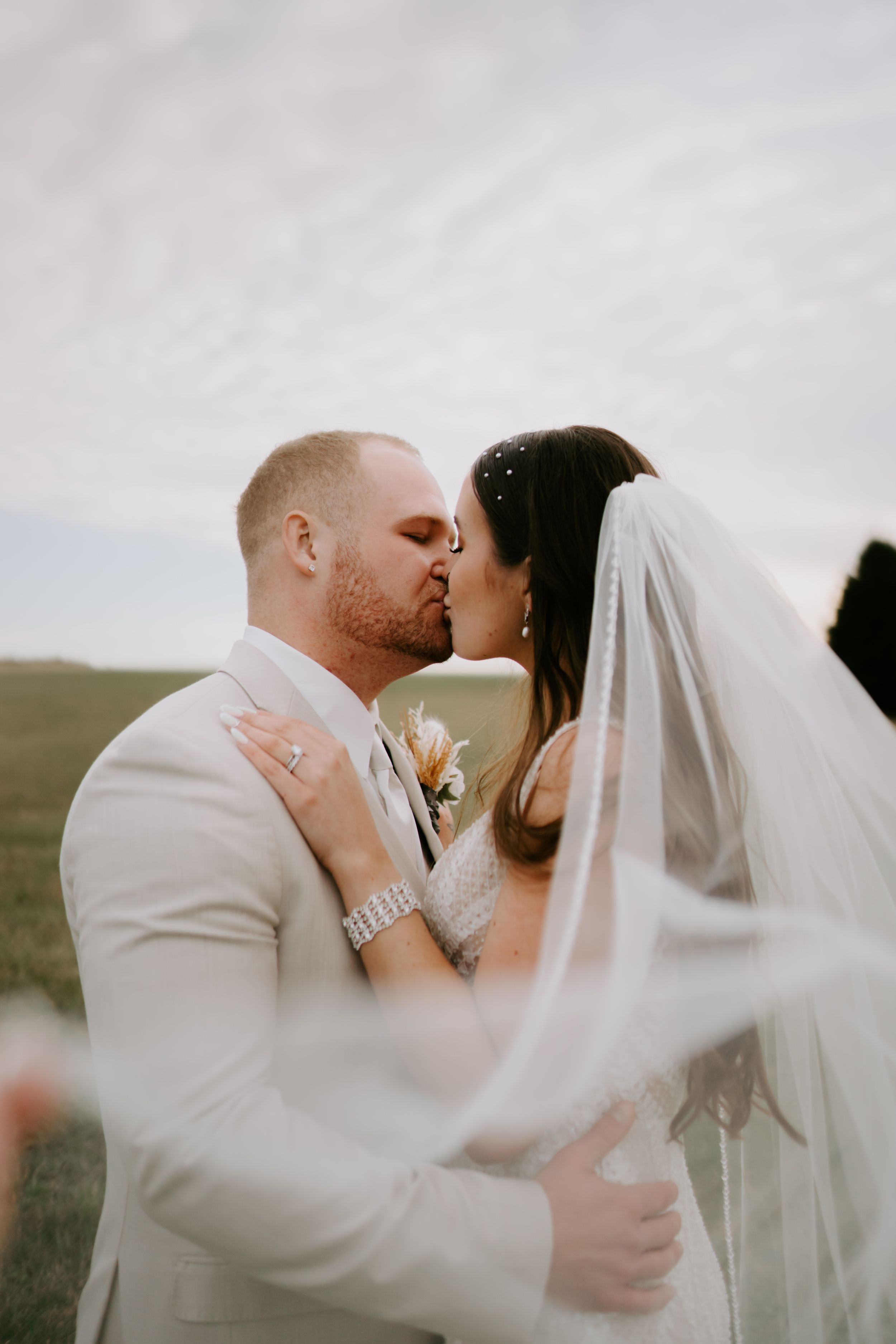 Intimate wedding portrait of couple sharing tender moment against cloudy sky.