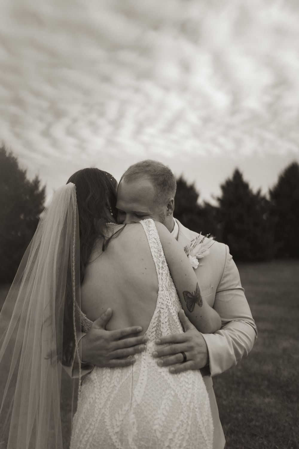 Black and white wedding photo capturing couple's emotional embrace outdoors.