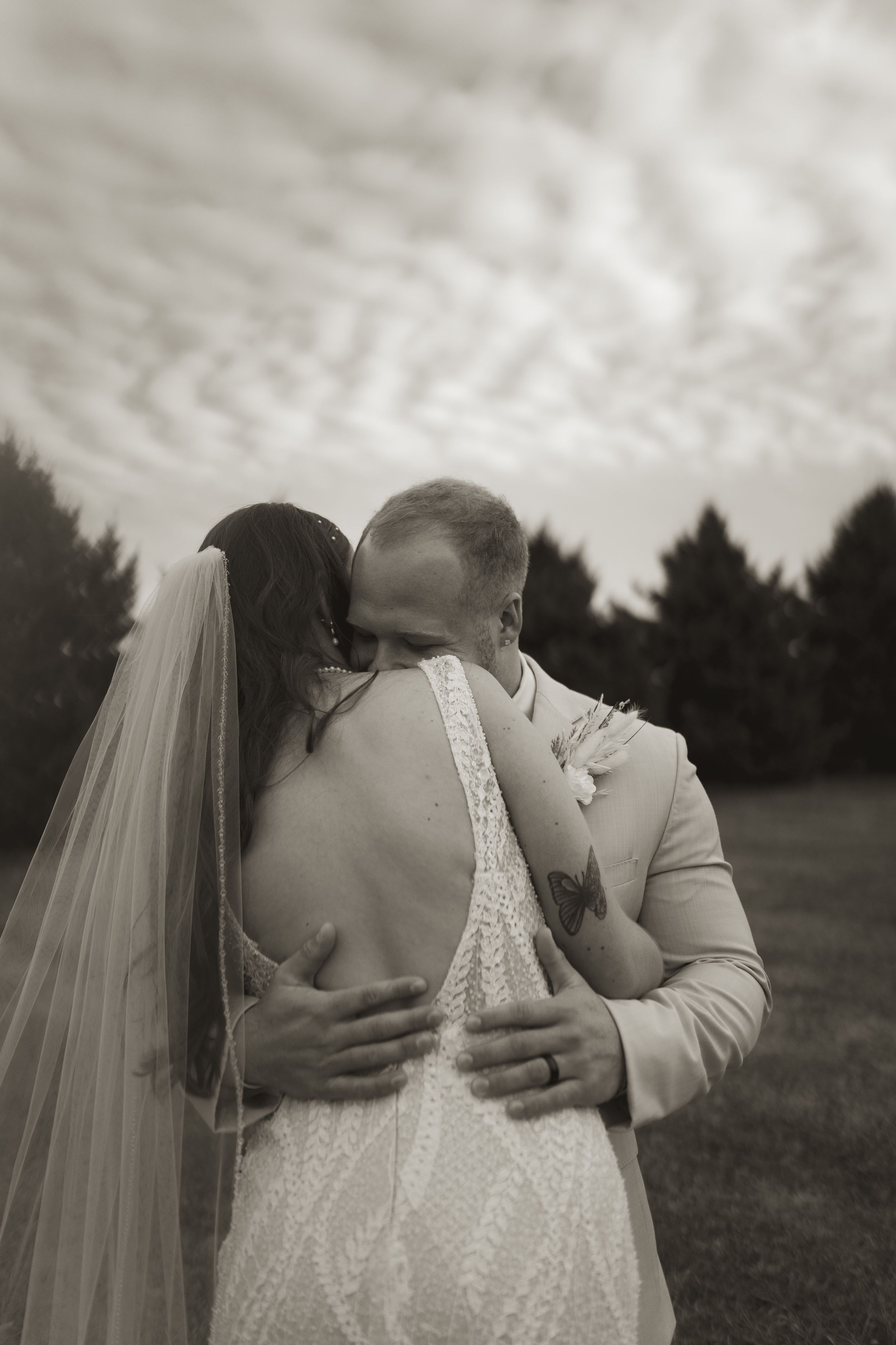 Black and white wedding photo capturing couple's emotional embrace outdoors.