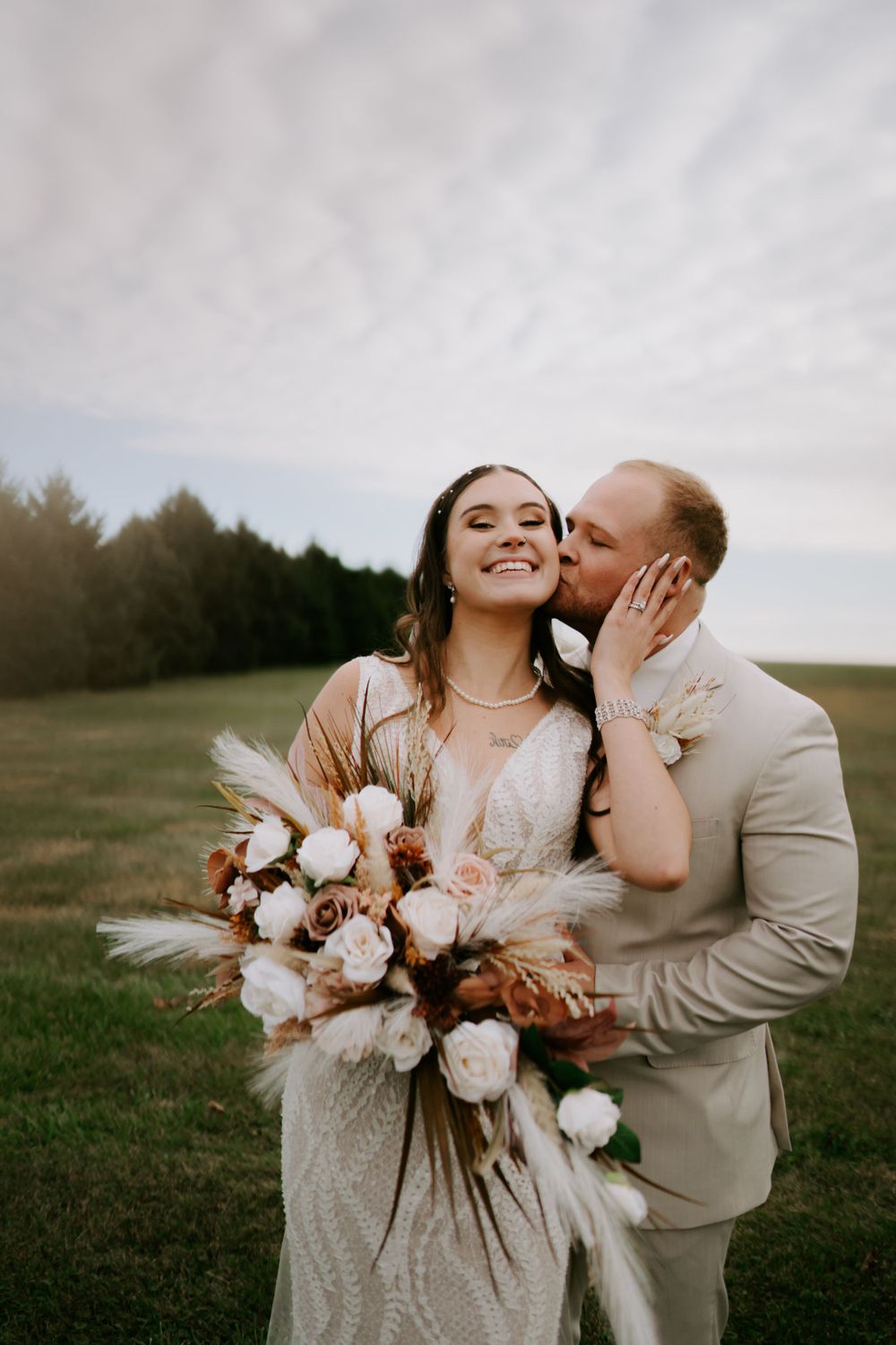Newlyweds share joyful moment with bride holding rustic bouquet in outdoor setting.