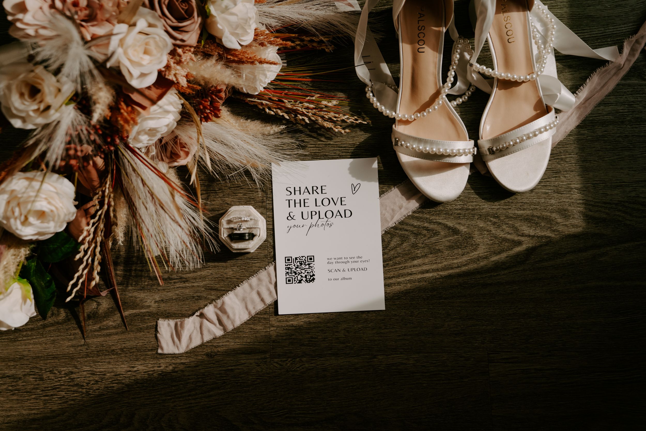 Wedding details including bridal accessories and floral arrangements on dark wooden surface.