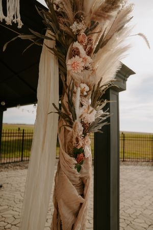 Modern wedding arch decorated with flowing fabric and dried floral arrangements.