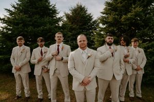 Groomsmen in light colored suits pose together outdoors.