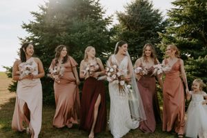Wedding party in shades of pink and burgundy dresses stand together against evergreen trees.