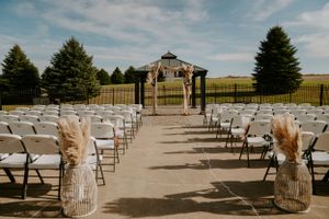 White ceremony chairs arranged in rows with pampas grass aisle decorations at outdoor venue.