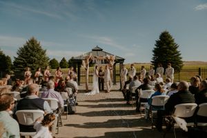 Outdoor wedding venue with stone walls and guests gathered under blue skies.