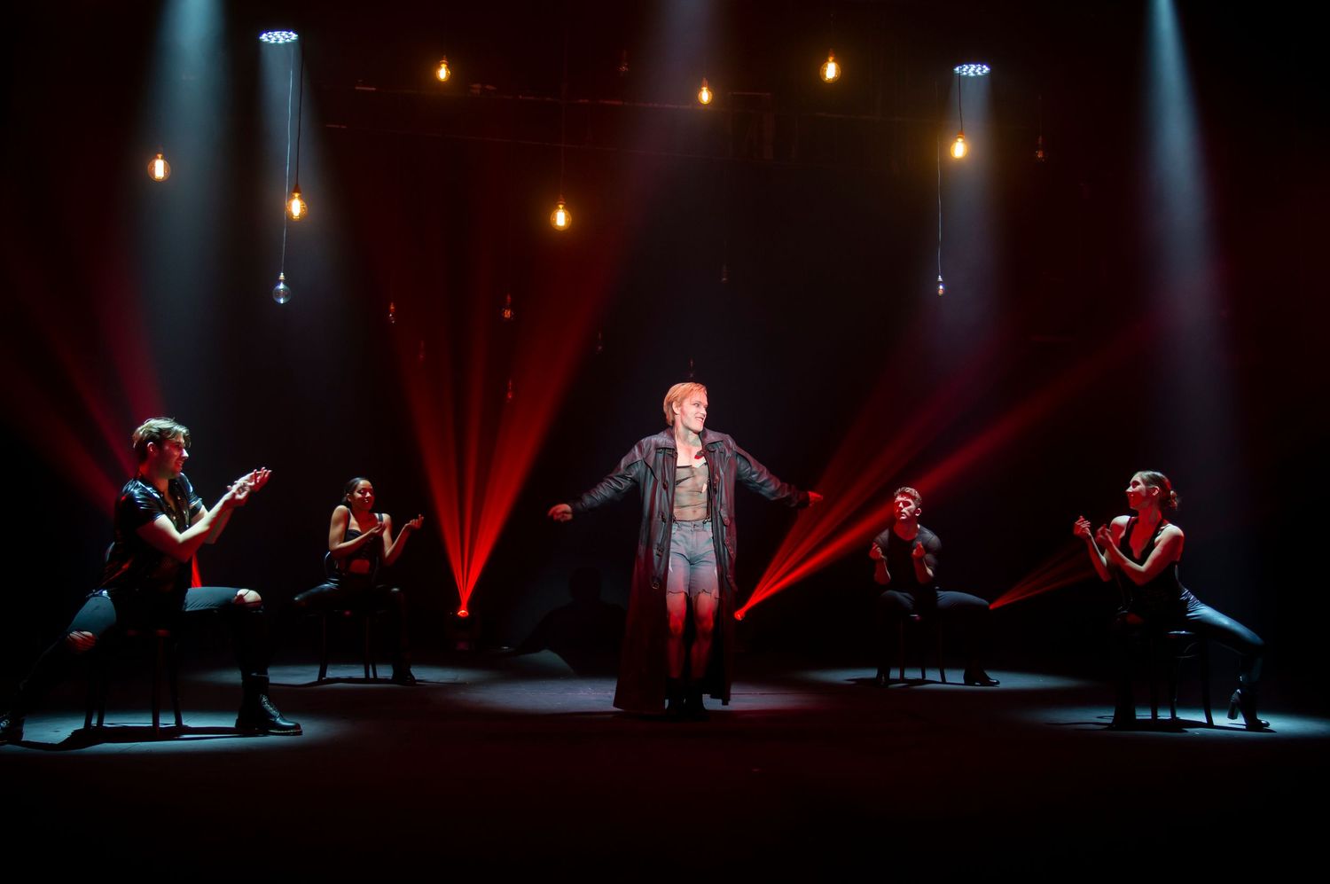 Dramatic stage performance with red spotlights and performers in silhouette.