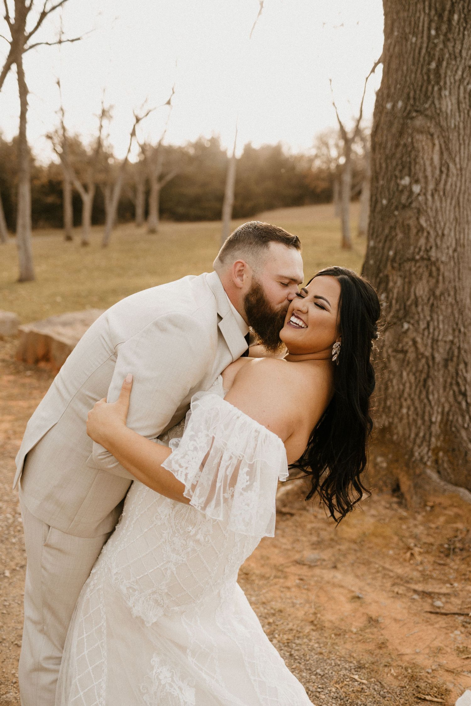 A romantic moment between a couple in wedding attire posing in a rustic outdoor setting at sunset.