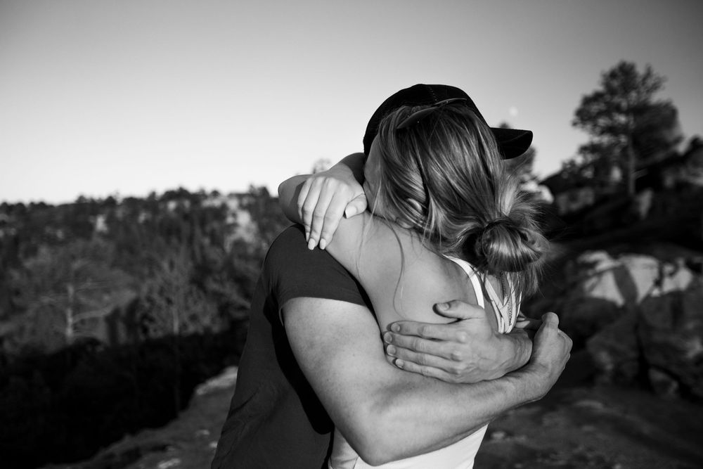 An intimate black and white moment shows two people hugging outdoors.
