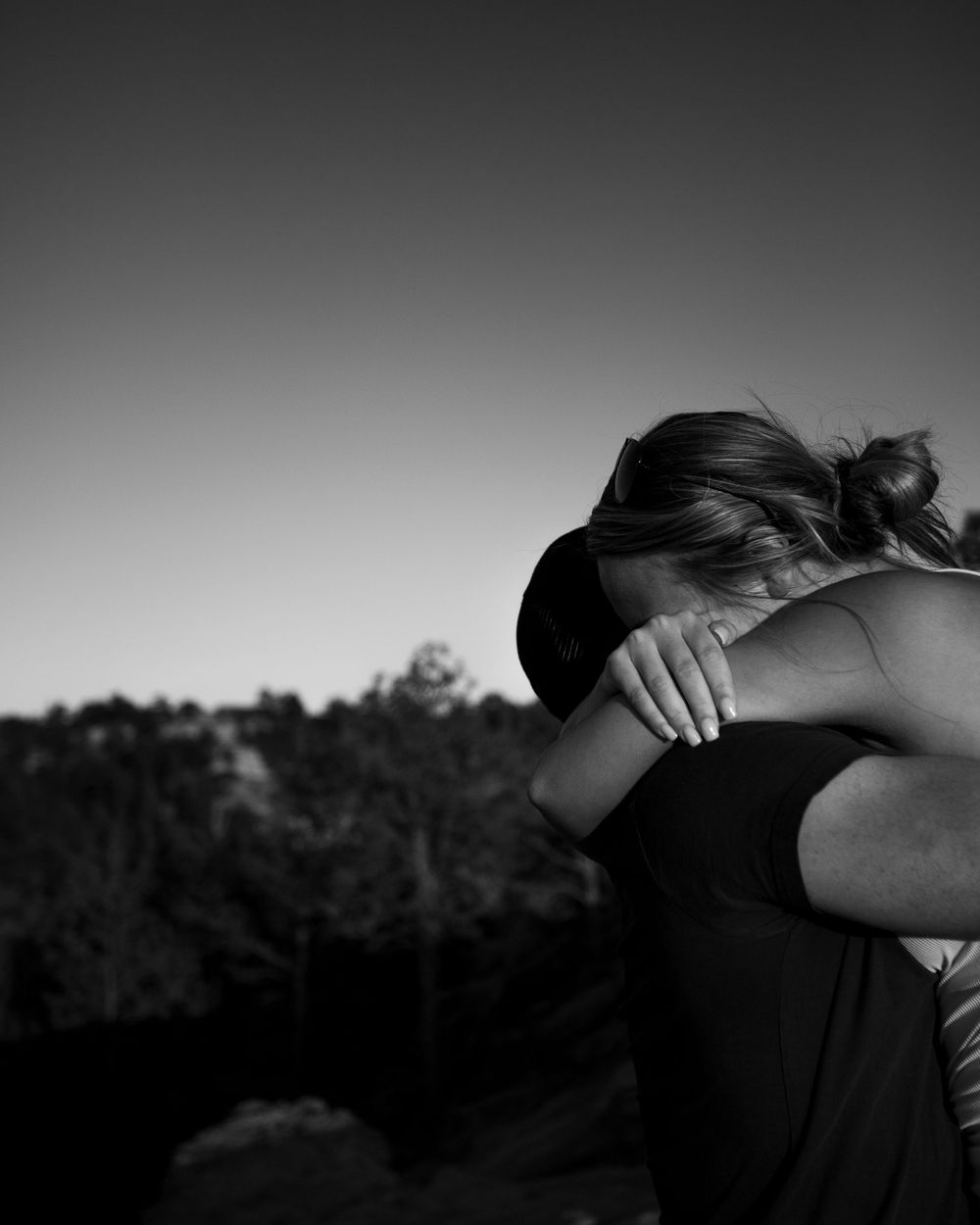 A couple embraces emotionally against a scenic mountain backdrop in black and white.