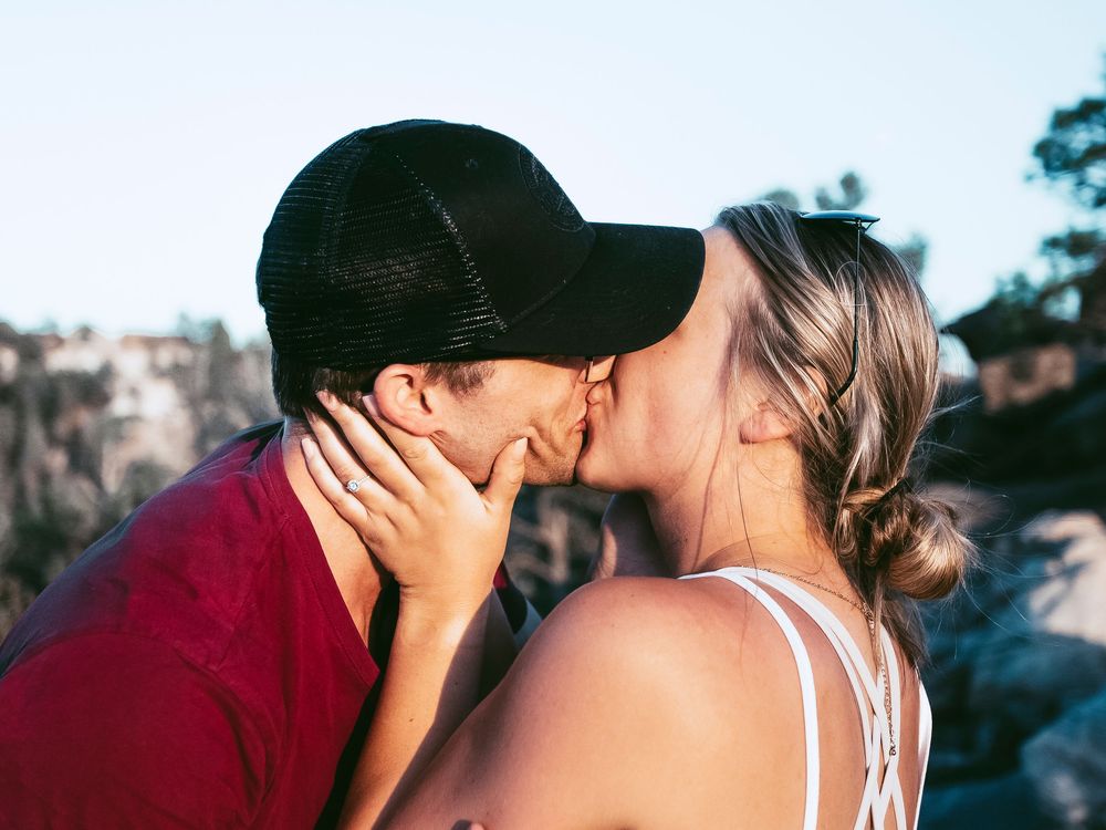 A tender kiss shared between a couple wearing casual attire outdoors.