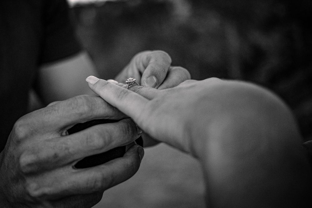 Close-up black and white shot of hands during a proposal moment.