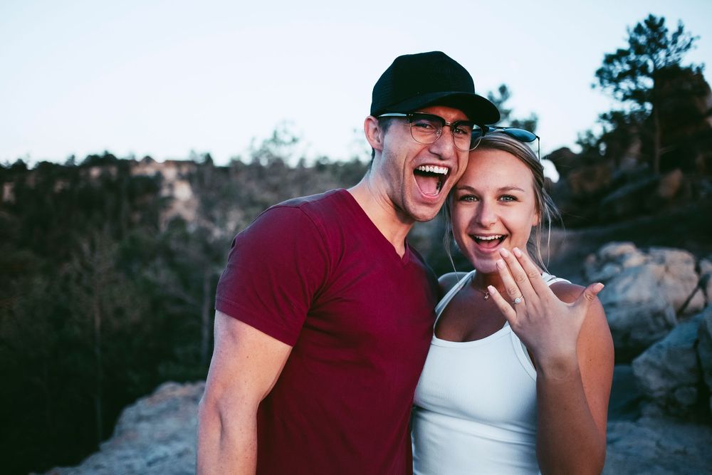 A joyful couple celebrates their engagement outdoors while showing off the ring.