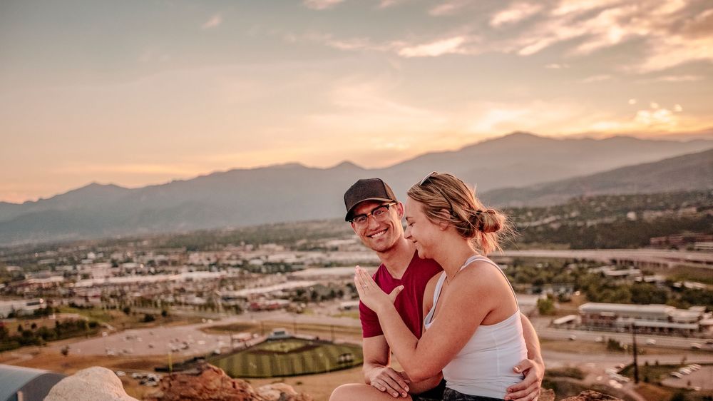 A loving couple shares a sunset moment with mountain views in the background.