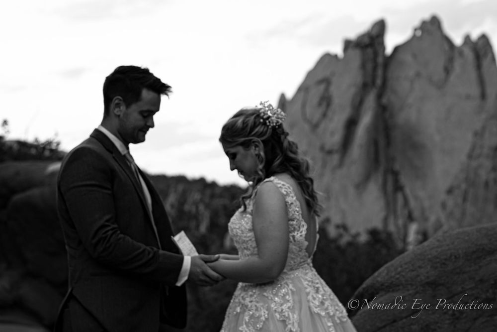 A wedding couple exchanges vows in front of dramatic rock formations in black and white.