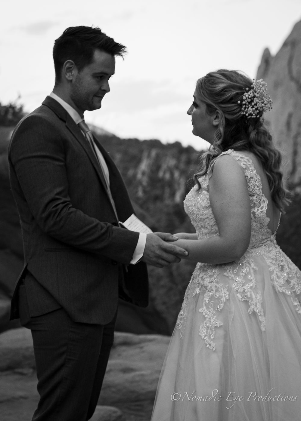 Bride and groom hold hands during their wedding ceremony against a mountain backdrop.