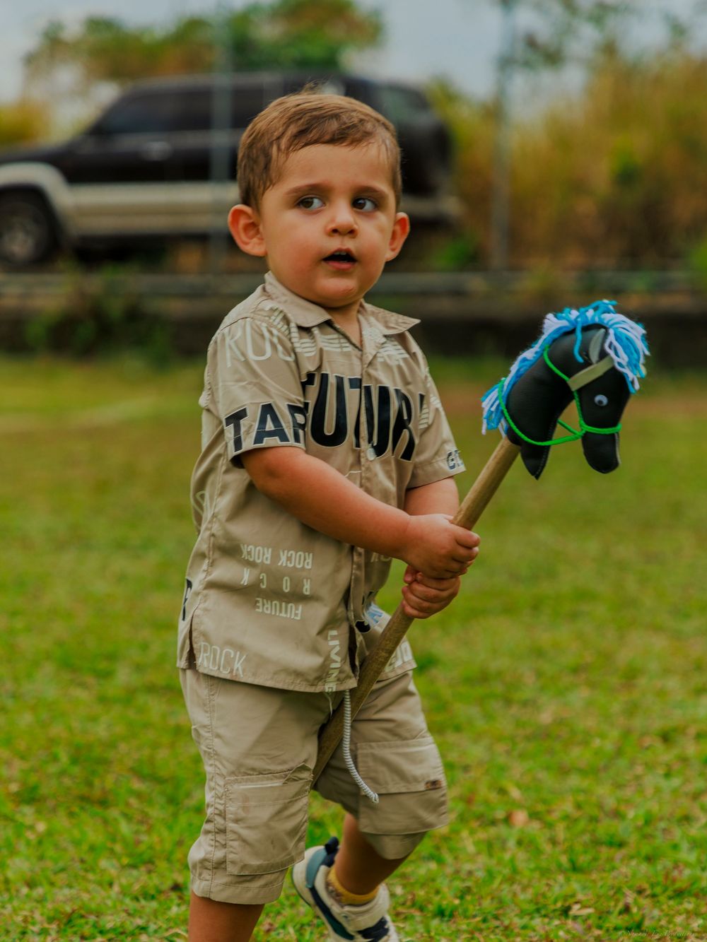 Young child in beige outfit plays outdoors holding a blue toy.