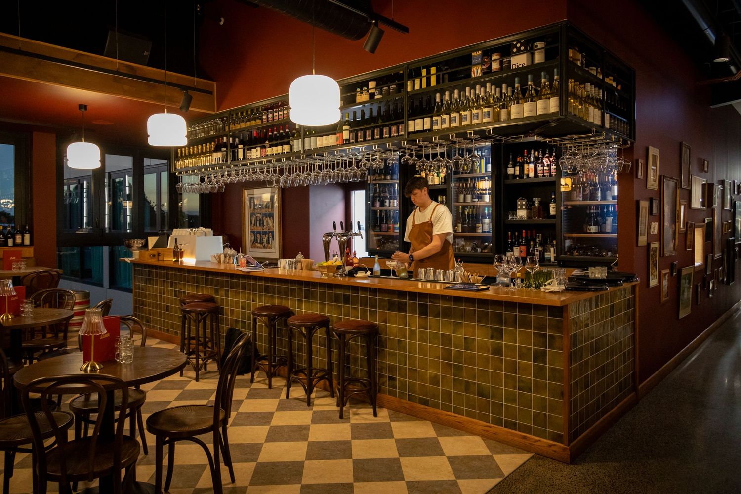 Warm, welcoming bar with shelves of wine bottles, checked floors, and patrons enjoying drinks at night.