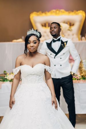 A bride in a stunning ball gown poses with her groom in a white tuxedo jacket.