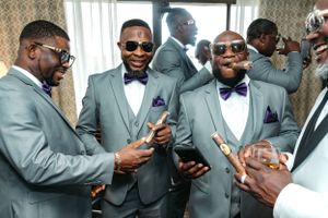 Groomsmen in gray suits and bowties share a laugh during wedding preparations.
