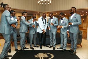 Wedding party members in light blue suits gather together at an indoor venue with one member wearing a white suit jacket.