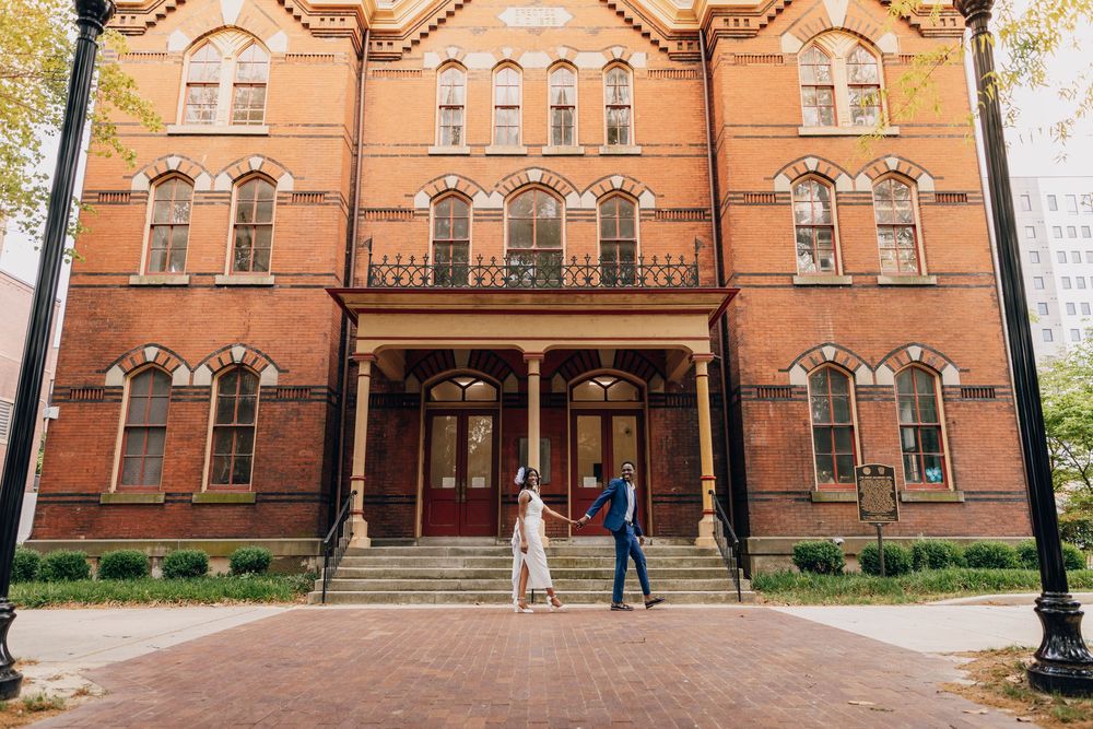 Couple holding hands in front of a historic red brick building with arched windows during an outdoor engagement session.