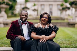 Couple in formal attire poses on grass in front of elegant building.